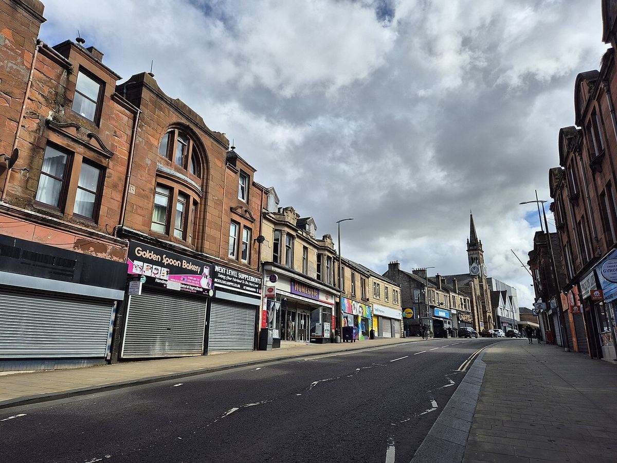 Main Street, Wishaw, with sandstone tenements above shops and a church spire in the distance